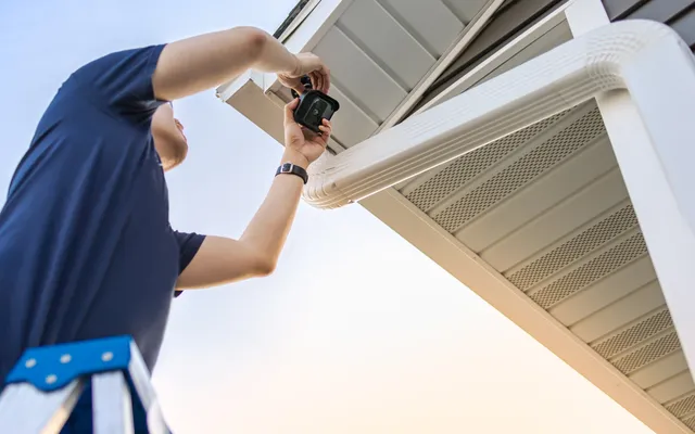 Technician installing an outdoor security camera under the eave of a home